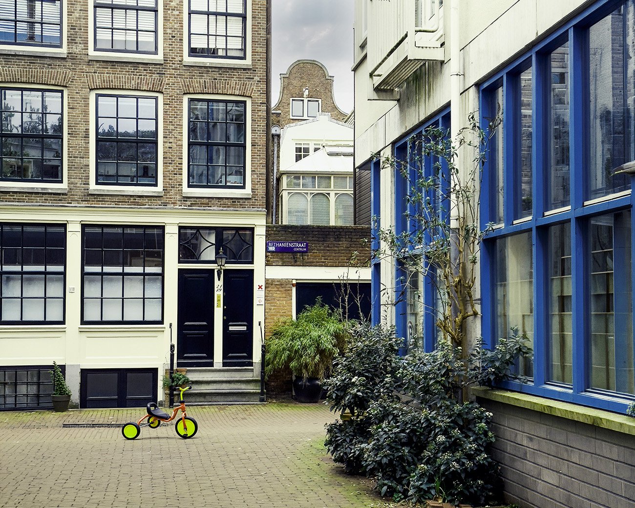 Amsterdamse binnenplaats met gesloten voordeuren en een kinderfiets op de stoep