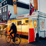 Friteskraam en fietsers op de Albert Cuypmarkt in Amsterdam tijdens de avondspits