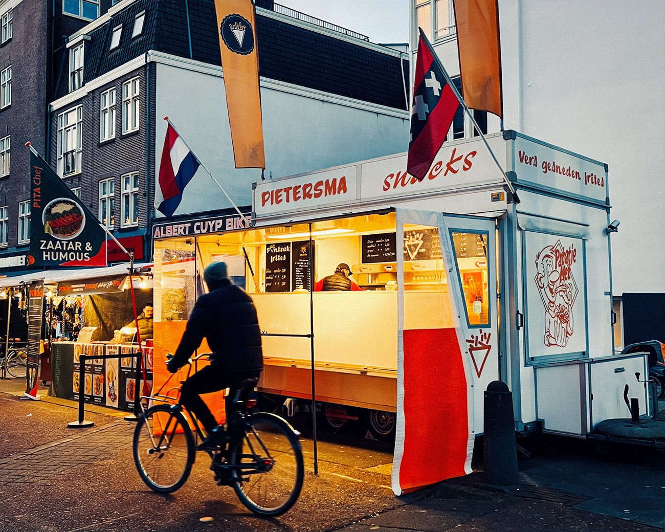 Friteskraam en fietsers op de Albert Cuypmarkt in Amsterdam tijdens de avondspits