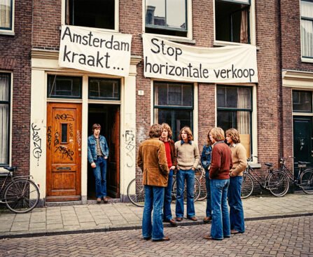 Jonge activisten staan voor een Amsterdams woonhuis met spandoeken “Amsterdam kraakt” en “Stop horizontale verkoop”, symbool van de kraakbeweging en de strijd om betaalbare huisvesting.