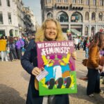 Demonstrant op de Dam in Amsterdam met een bord “We should all be feminists” tijdens een feministische bijeenkomst.