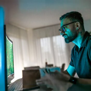 Man kijkt geconcentreerd naar een computerscherm met groene code terwijl het schermlicht zijn gezicht verlicht.
