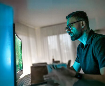 Man kijkt geconcentreerd naar een computerscherm met groene code terwijl het schermlicht zijn gezicht verlicht.