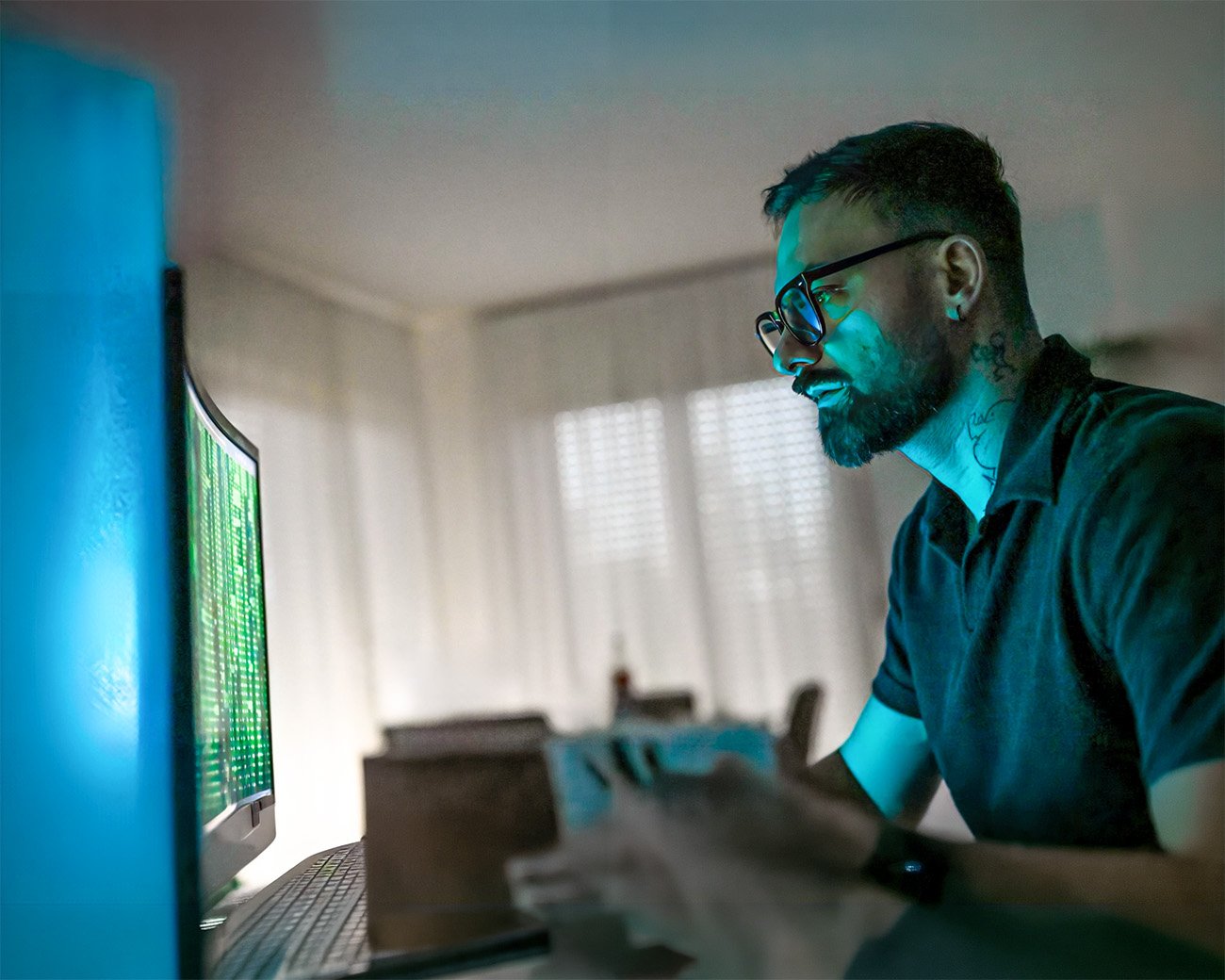 Man kijkt geconcentreerd naar een computerscherm met groene code terwijl het schermlicht zijn gezicht verlicht.