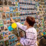 Vrouw legt bloemen bij een herdenkingsmuur met foto’s van gesneuvelde Oekraïense soldaten