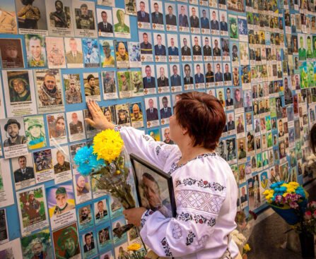 Vrouw legt bloemen bij een herdenkingsmuur met foto’s van gesneuvelde Oekraïense soldaten