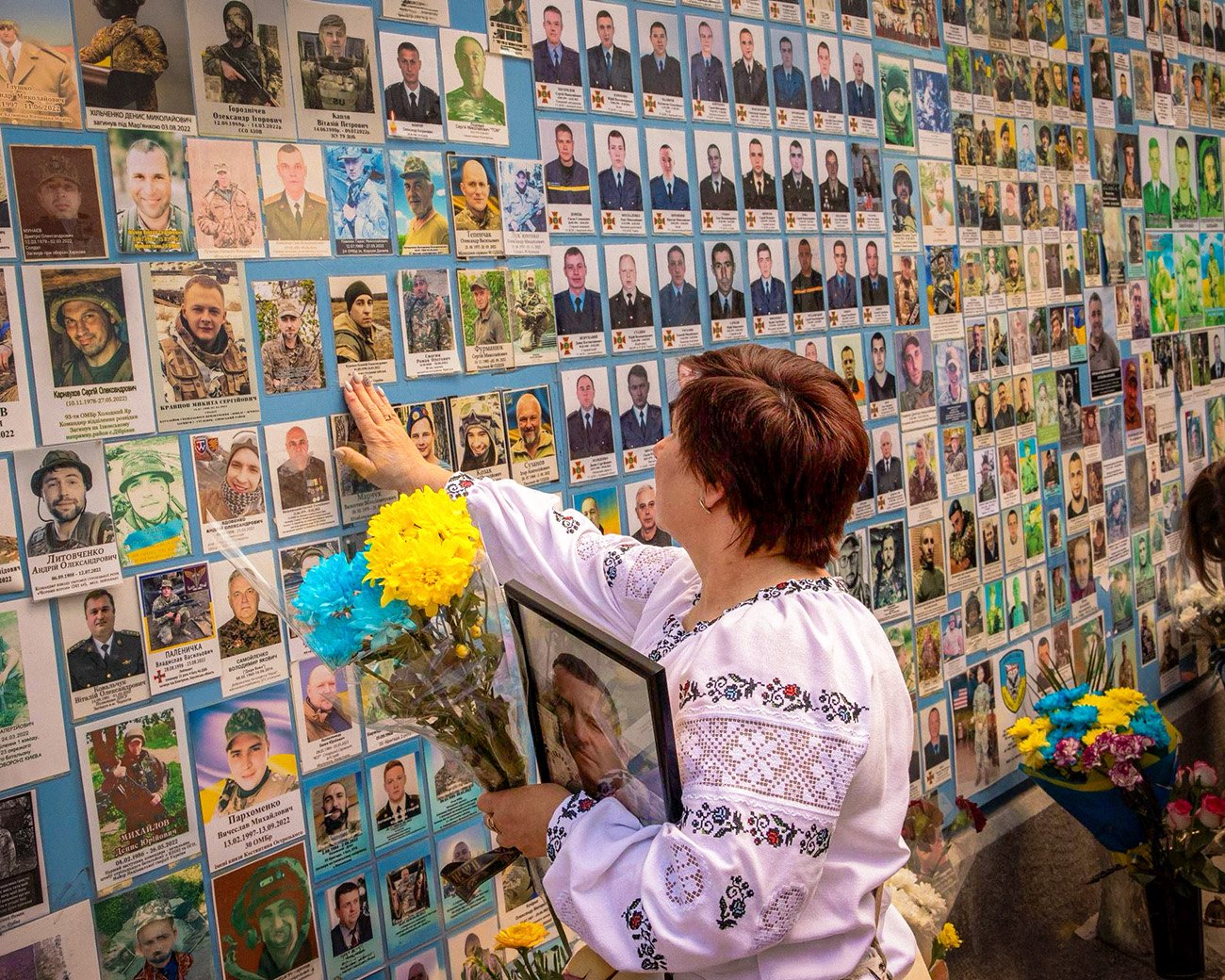 Vrouw legt bloemen bij een herdenkingsmuur met foto’s van gesneuvelde Oekraïense soldaten