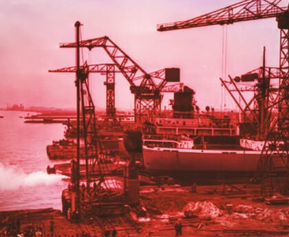 Scheepswerf aan het IJ in Amsterdam-Noord met kranen, een schip in aanbouw en industriële bedrijvigheid langs de oever.