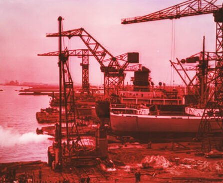 Scheepswerf aan het IJ in Amsterdam-Noord met kranen, een schip in aanbouw en industriële bedrijvigheid langs de oever.