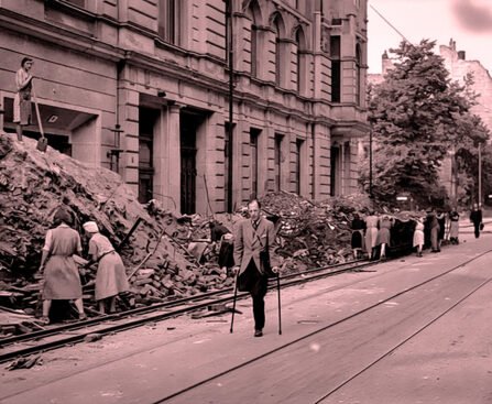 Mensen ruimen puin in een verwoeste Duitse stad na de Tweede Wereldoorlog terwijl een man met krukken door de straat loopt