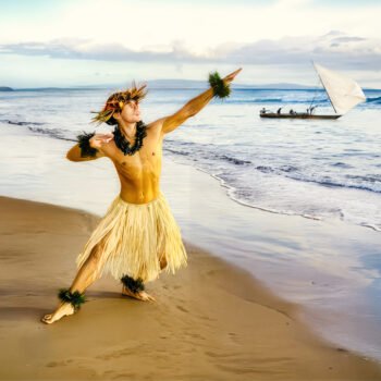 Persoon in traditionele kledij aan de kust van Guam met een zeilkano op zee, als verwijzing naar CHamoru cultuur, zeevaart en zelfbeschikking.