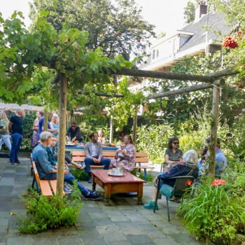 Buurtgenoten zitten en staan samen in een groene binnentuin bij Plan C aan het Smaragdplein in de Diamantbuurt.