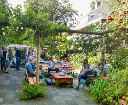 Buurtgenoten zitten en staan samen in een groene binnentuin bij Plan C aan het Smaragdplein in de Diamantbuurt.
