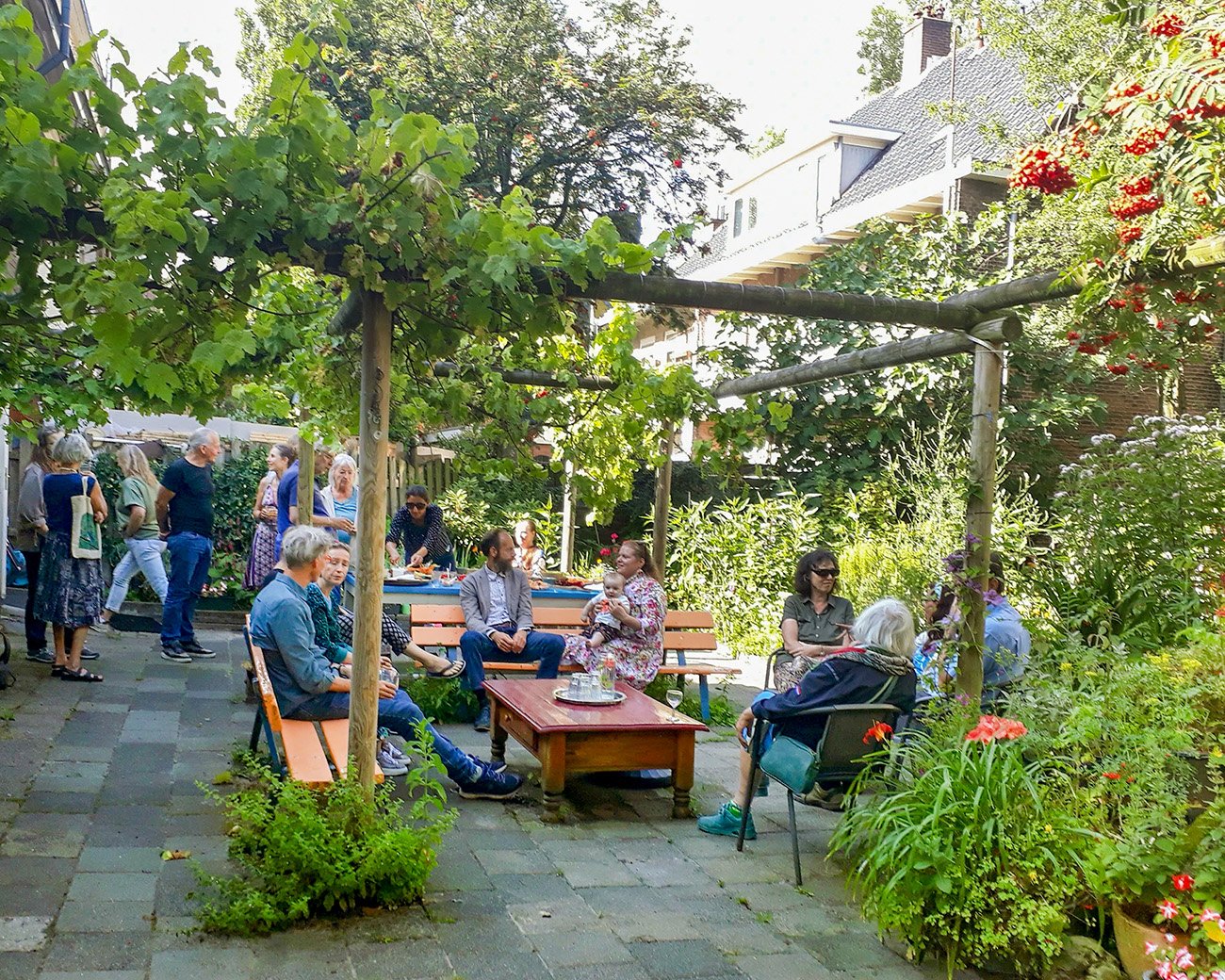 Buurtgenoten zitten en staan samen in een groene binnentuin bij Plan C aan het Smaragdplein in de Diamantbuurt.