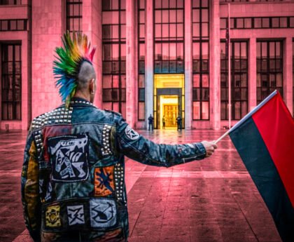 Een demonstrant met een rood-zwarte vlag staat voor een verlicht overheidsgebouw, terwijl de spanning tussen protest, autonomie en institutionele macht zichtbaar wordt.