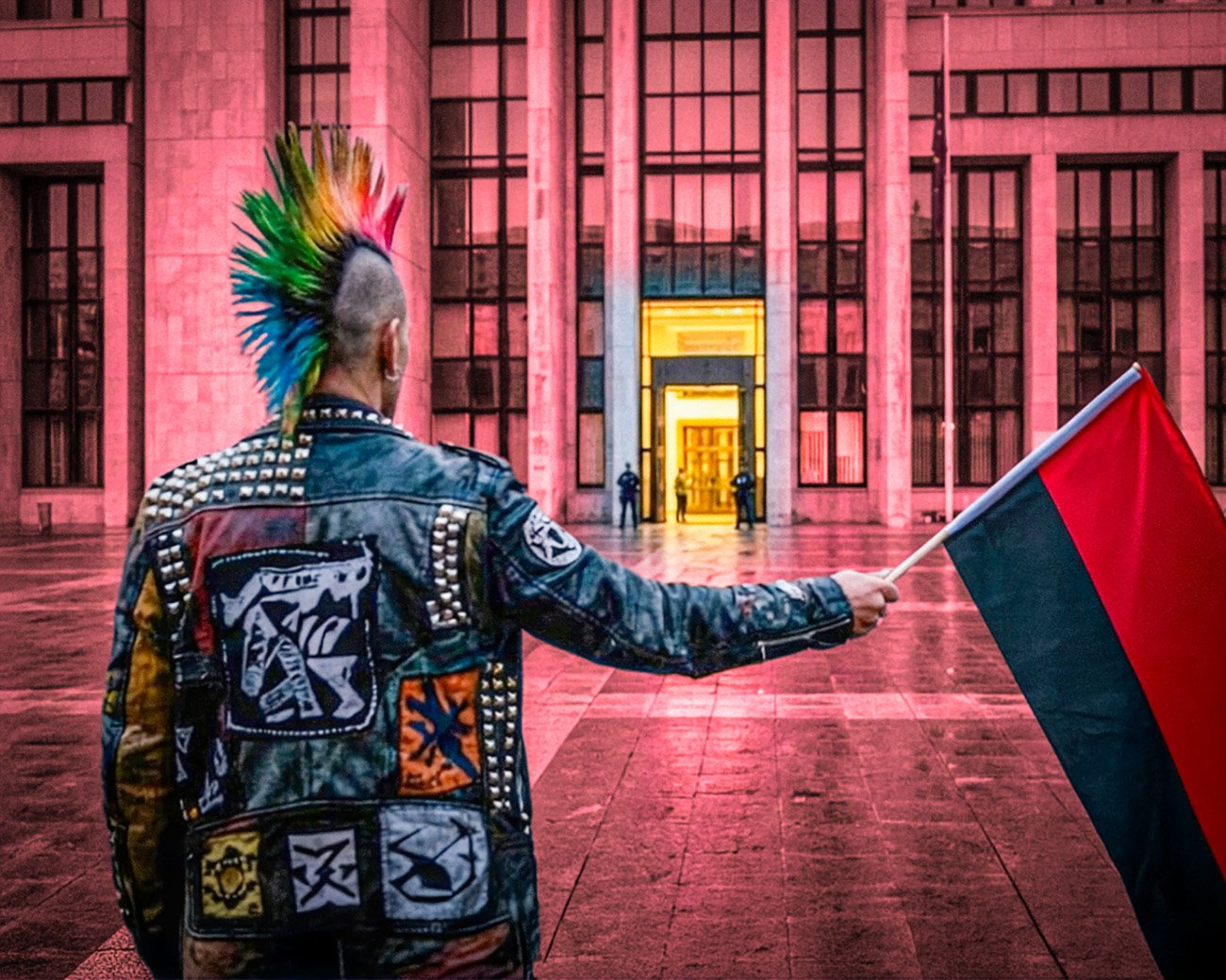 Een demonstrant met een rood-zwarte vlag staat voor een verlicht overheidsgebouw, terwijl de spanning tussen protest, autonomie en institutionele macht zichtbaar wordt.