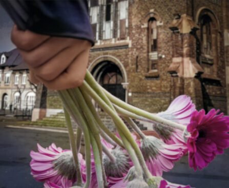 Hand met roze bloemen voor de Saint-Amé-kerk in Liévin, waar de mijnwerkersramp van 1974 wordt herdacht.