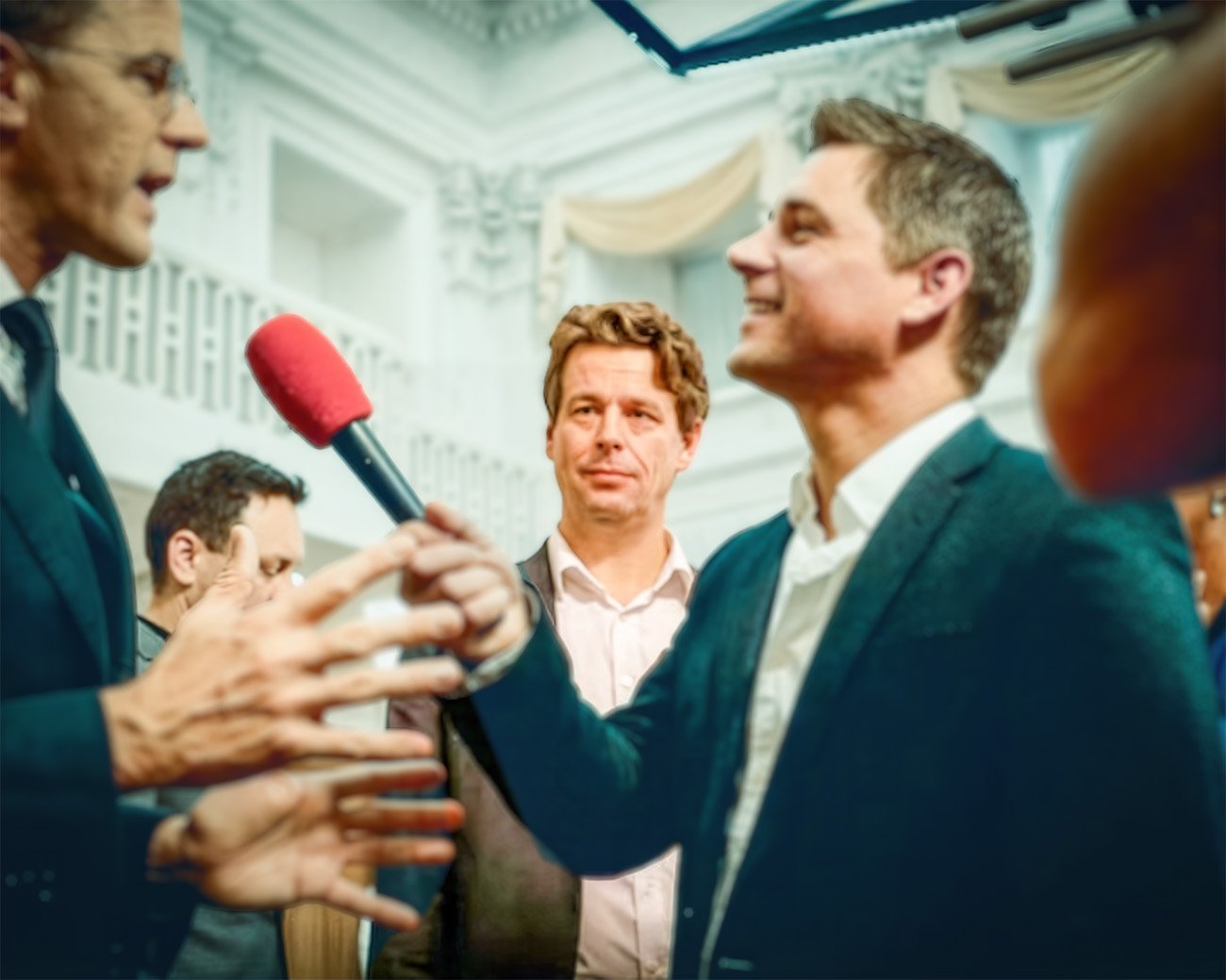 Journalist houdt een microfoon bij politici en omstanders in een politieke omgeving, tijdens een gesprek over media en macht.