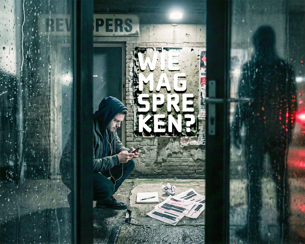 Een jonge man zit met telefoon bij een redactiekantoor, terwijl op de muur achter hem “Wie mag spreken?” staat.