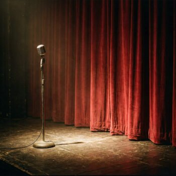Microfoon op een leeg podium voor een gesloten rood gordijn, als beeld voor literatuur, weigering en de normalisering van geweld.