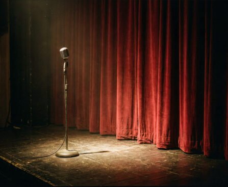 Microfoon op een leeg podium voor een gesloten rood gordijn, als beeld voor literatuur, weigering en de normalisering van geweld.