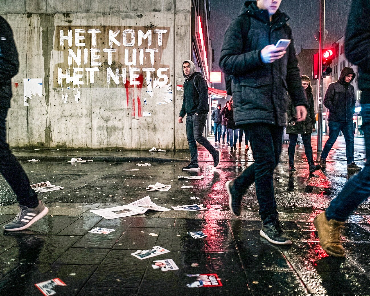 Mensen lopen over een natte stadsstraat terwijl op een muur “Het komt niet uit het niets” staat.