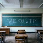 Leeg Amerikaans klaslokaal met op het schoolbord de tekst “Who you with?” en een Amerikaanse vlag aan de muur.