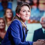 Politicus aan een talkshowtafel met publiek op de achtergrond, tijdens een gesprek over persoonlijke verhalen en politieke macht.