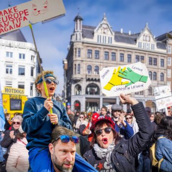 Demonstranten in Amsterdam houden borden omhoog tegen fascisme en voor samenleven, met een kind op iemands schouders op de voorgrond.