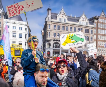 Demonstranten in Amsterdam houden borden omhoog tegen fascisme en voor samenleven, met een kind op iemands schouders op de voorgrond.
