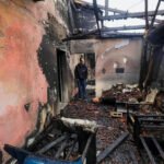 Palestijnse man staat tussen verbrande muren, verkoolde balken en puin in een huis na een aanval door Israëlische kolonisten in Fundokumiyya.