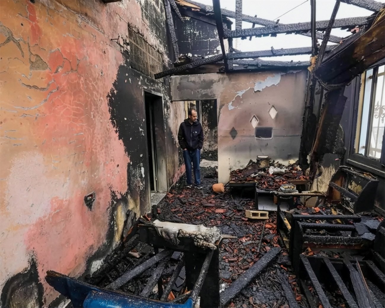 Palestijnse man staat tussen verbrande muren, verkoolde balken en puin in een huis na een aanval door Israëlische kolonisten in Fundokumiyya.