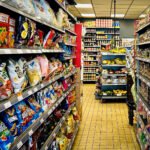 Supermarktpad vol zakken chips, snacks en bewerkte voeding, met een kleine fruit- en groenteafdeling op de achtergrond.