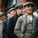Groep arbeiders met petten en jassen staat dicht op elkaar bij een gebouw in het East End rond 1930.