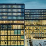 Verlicht kantoorgebouw met veel ramen, als beeld voor financiële macht, belastingroutes en besluiten achter gesloten deuren.