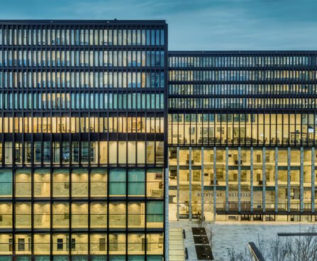 Verlicht kantoorgebouw met veel ramen, als beeld voor financiële macht, belastingroutes en besluiten achter gesloten deuren.