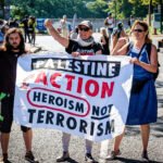 Drie demonstranten houden een spandoek vast met de tekst “Palestine Action, heroism not terrorism” tijdens een protest op straat.