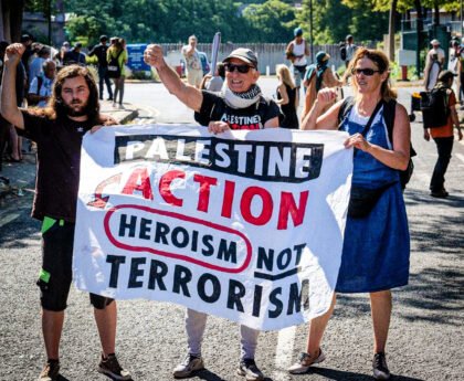 Drie demonstranten houden een spandoek vast met de tekst “Palestine Action, heroism not terrorism” tijdens een protest op straat.