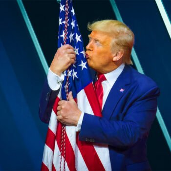 Donald Trump kust een Amerikaanse vlag tijdens een politieke bijeenkomst.
